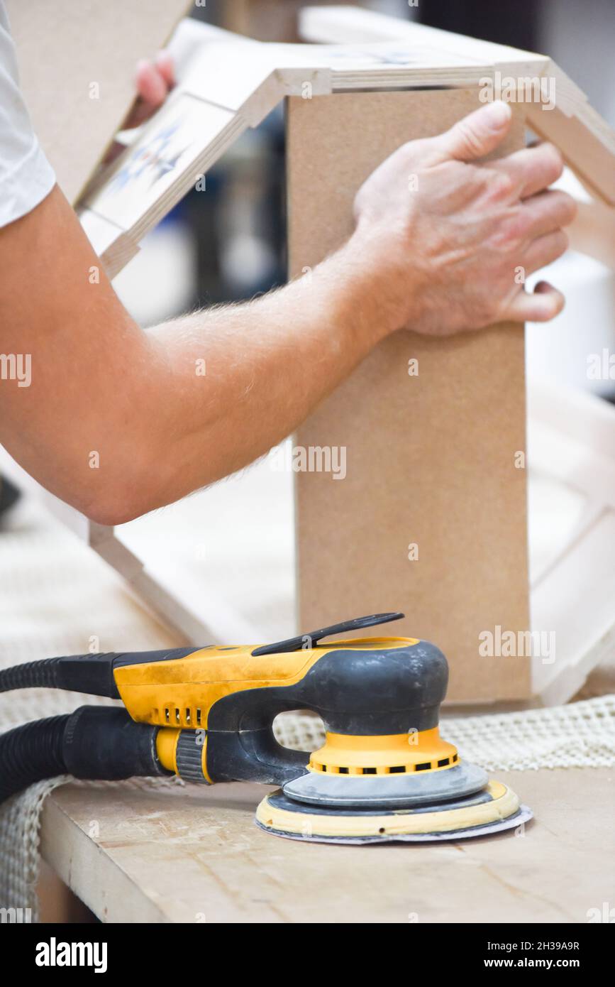 Ein Mann, der mit einem Elektroschleifer für Elektrowerkzeuge Holz in der Tischlerei basteln kann Stockfoto