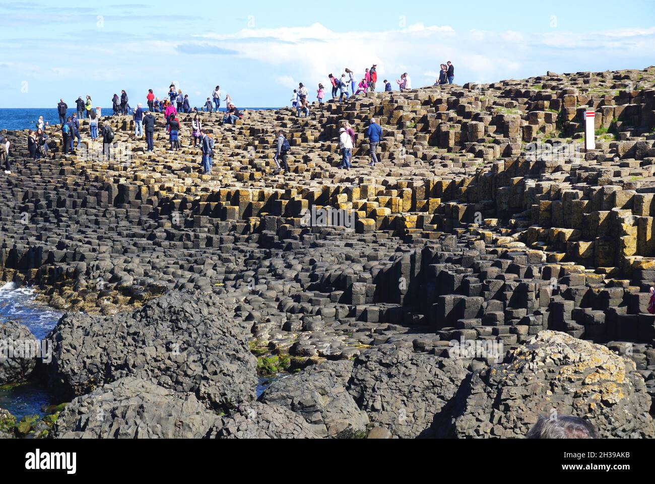 Besucher klettern auf natürliche vulkanische Felsformationen am Giant’s Causeway, der sich am Rande des Meeres an der Nordküste von Nordirland befindet. Stockfoto