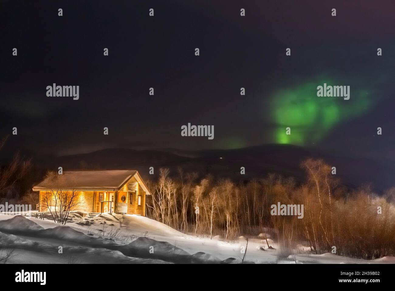 Nordlichter (Aurora borealis) über einem schwedischen Holzhäuschen im Winter, in der Nähe des Abisko-Nationalparks, Lappland, Schweden Stockfoto