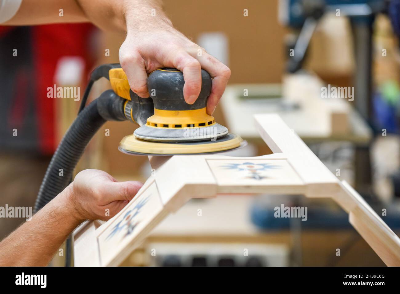 Ein Mann, der mit einem Elektroschleifer für Elektrowerkzeuge Holz in der Tischlerei basteln kann Stockfoto