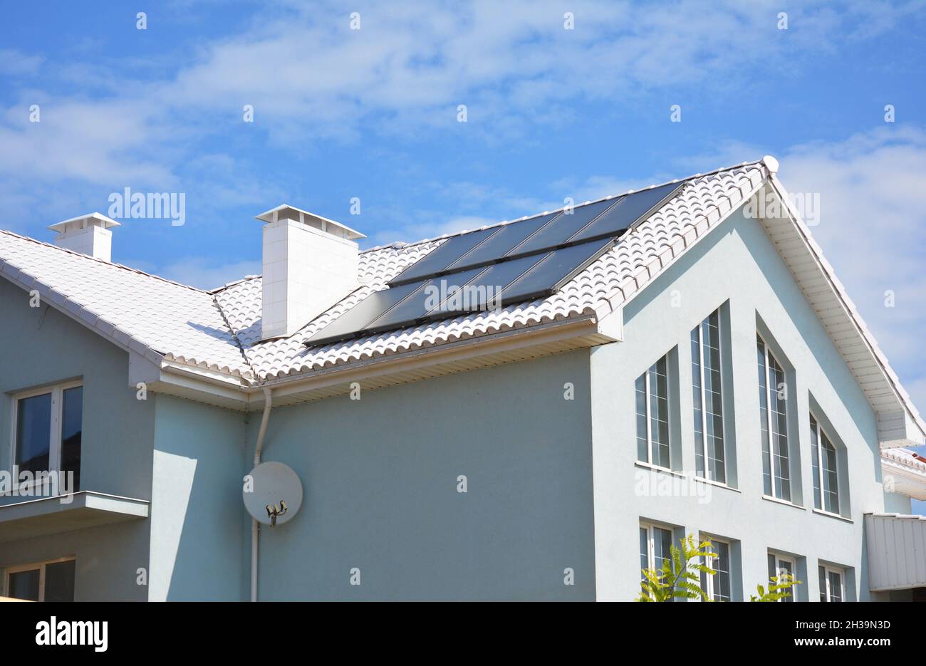 Weißes Ziegeldach aus Lehm und Sonnenkollektoren, solare Warmwasserbereitung für Energieeffizienz im Haus. Moderne Hauskonstruktion. Stockfoto
