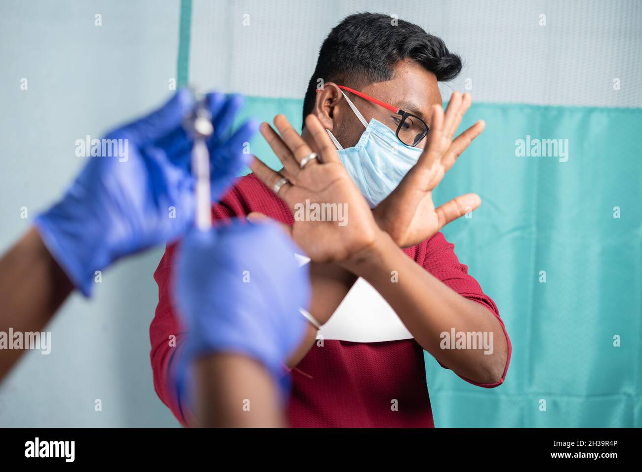 Selektive Fokussierung auf einen Mann mit medizinischer Gesichtsmaske, der Nein zur Covid-19- oder Coronavirus-Impfung sagt, indem er dem Arzt Handgesten zeigt - Konzept des Impfstoffs Stockfoto