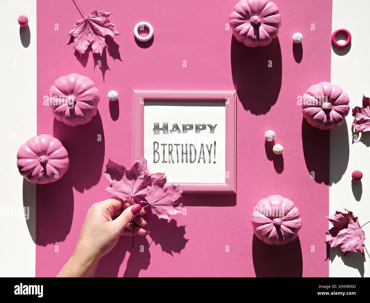 Happy Birthday Text im Rahmen mit Herbstdekor. Monochromatischer Look mit rosa Kürbissen und weiblichen Hand halten Herbst trockene Blätter rosa gemalt. Magenta Stockfoto