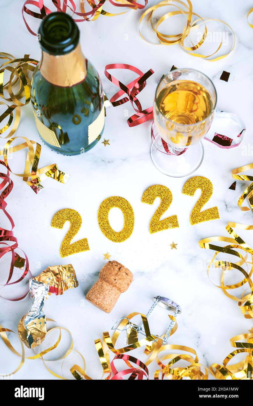 Frohes Neues Jahr 2022. Silvester Feier Konzept Hintergrund.Champagner-Flasche mit Glas und Konfetti auf Marmortisch.Selektive Fokus Stockfoto