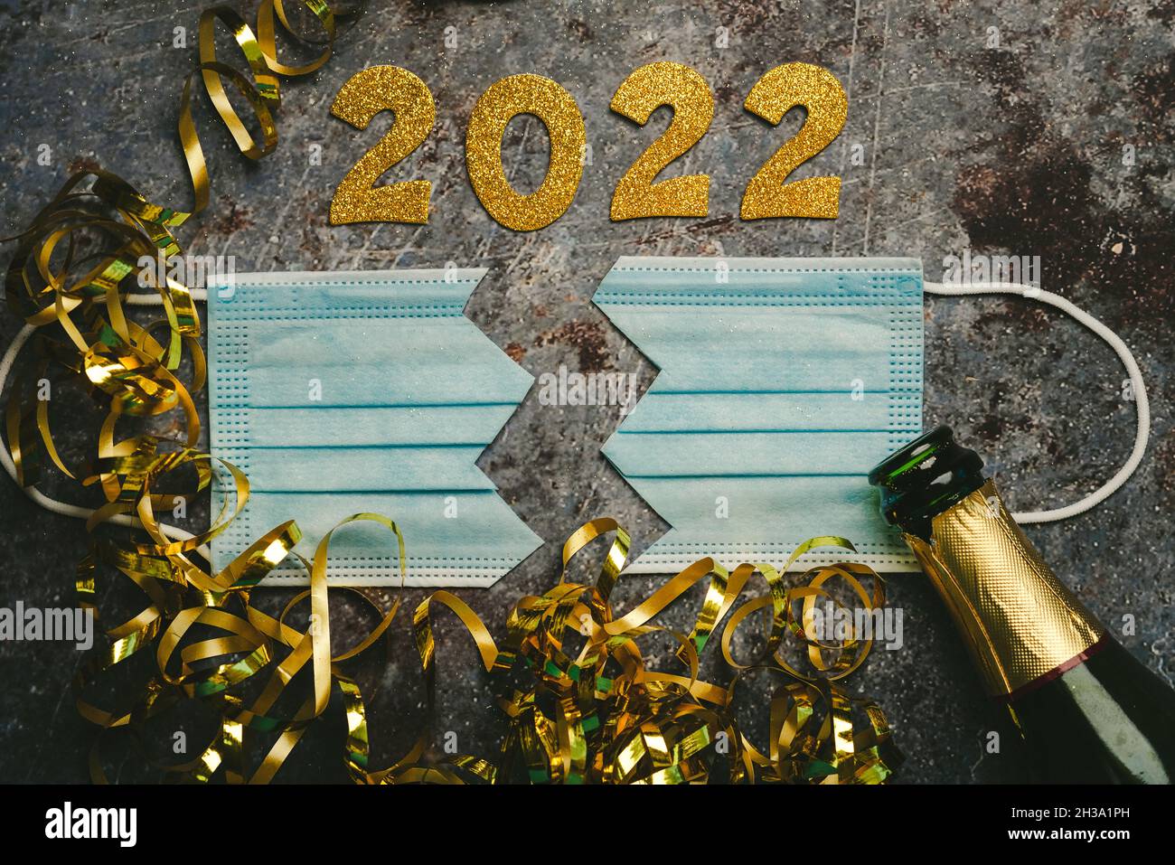 Silvester Feier Konzept Hintergrund.Schutz OP-Maske in zwei mit den Zahlen geteilt 2021 und Champagner-Flasche auf grauem Hintergrund. Konz Stockfoto