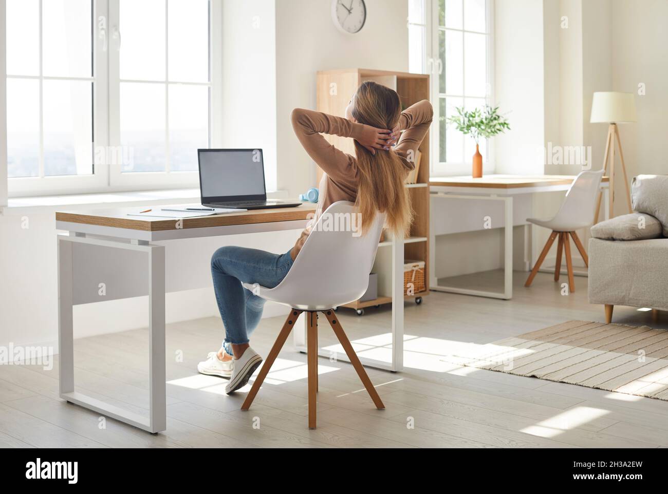 Die Studentin, die ihre Arbeit am Laptop beendet hat, entspannt sich in einem bequemen Stuhl neben ihrem Schreibtisch Stockfoto