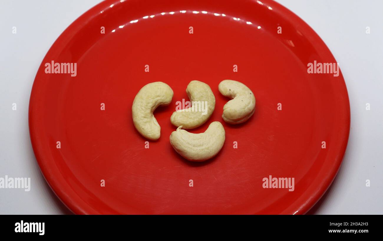 Vier Cashewnüsse befinden sich auf einem weißen Hintergrund auf einem roten Teller Stockfoto