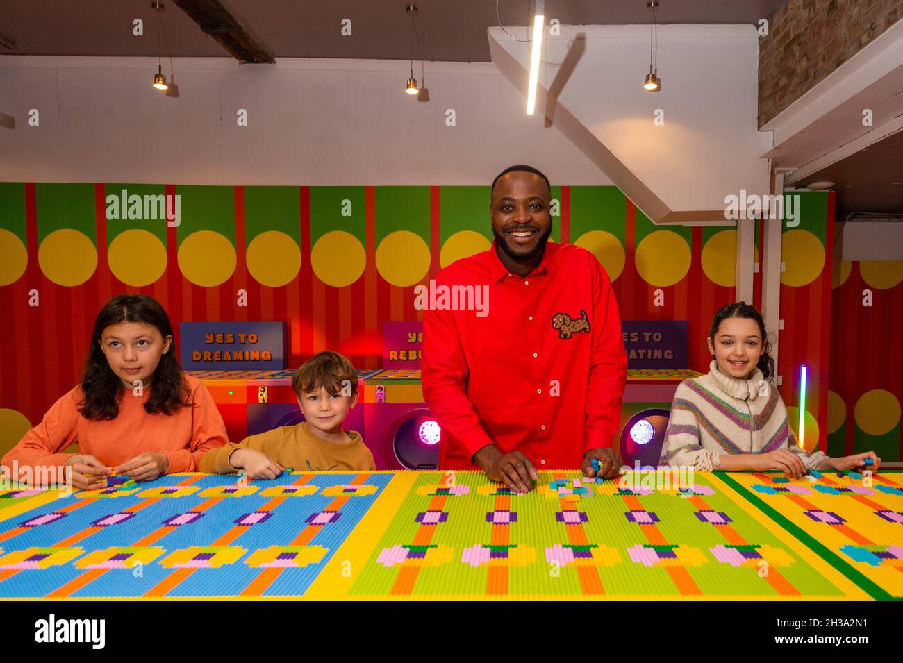 London, Großbritannien. 27. Oktober 2021. Einheimische Schulkinder enthüllen gemeinsam mit dem preisgekrönten Künstler und Designer Yinka Ilori seine neue Installation „Waschsalon der Träume“, in der er einen Gemeinschaftswaschtisch in seinem charakteristischen, farbenfrohen Stil neu gestaltet hat. Die Installation besteht aus über 200,000 LEGO Steinen und ist Teil der Kampagne „Rebuild the World“ der LEGO Gruppe, die Kinder als Meister der kreativen Problemlösung feiert. Sie kann in Bethnal Green Rd, Shoreditch, vom 28. Oktober bis 6. November 2021 gefunden werden. Kredit: Stephen Chung / Alamy Live Nachrichten Stockfoto