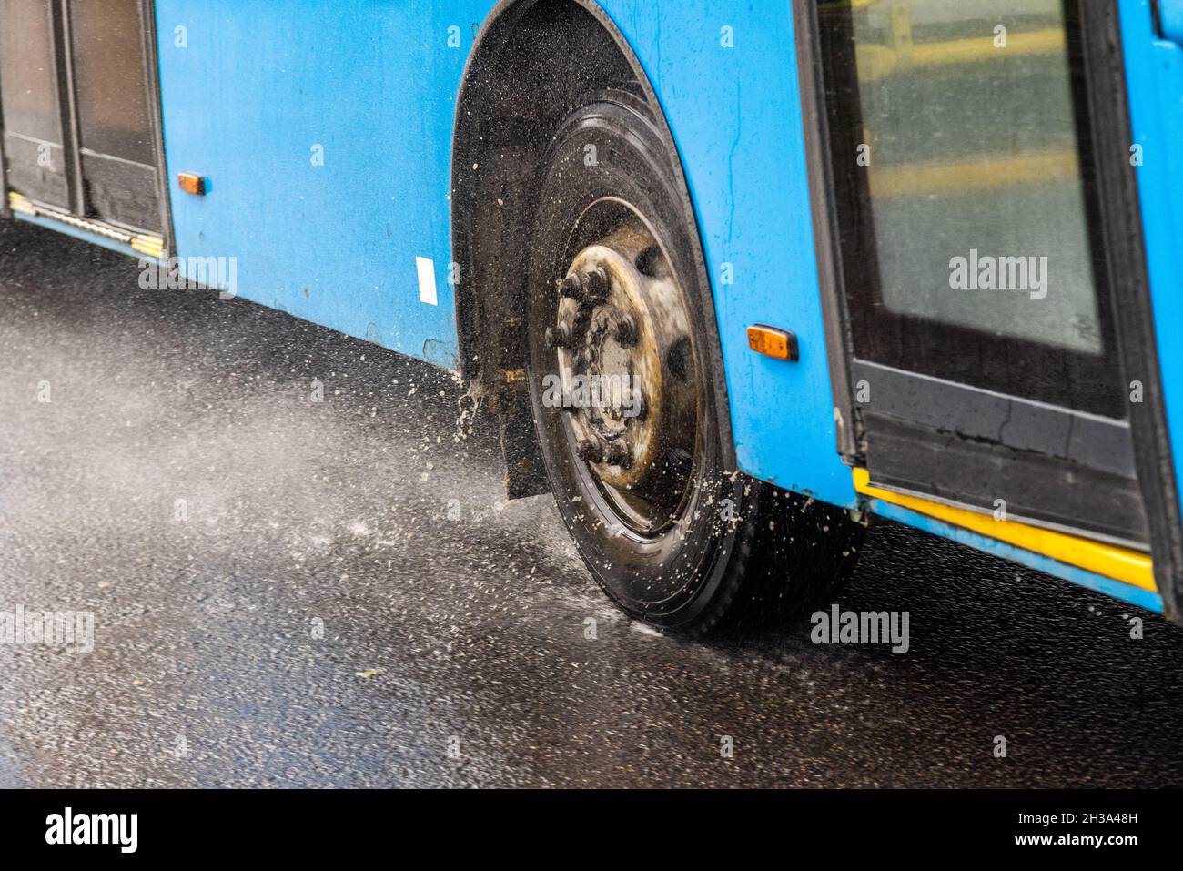 Blauer Stadtbus, der auf einer regnerischen Straße mit Wasserspritzern fährt Stockfoto