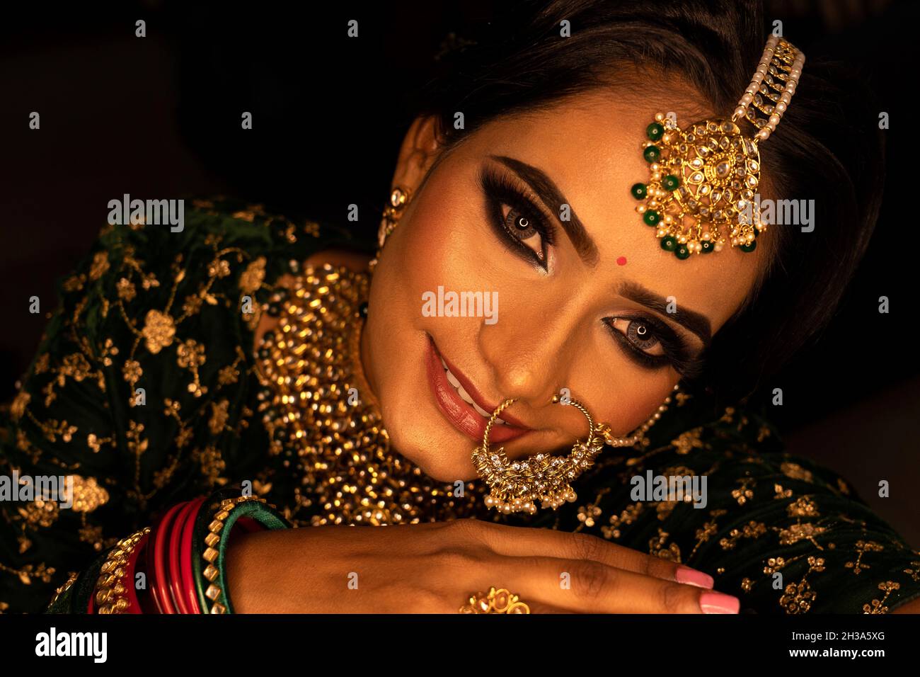 Frau Gesicht Nahaufnahme Porträt. Junge weibliche Modell in Sari Blick auf die Kamera. Tragen Sie grüne Armreifen und Schmuck. Schwarzer Hintergrund Stockfoto