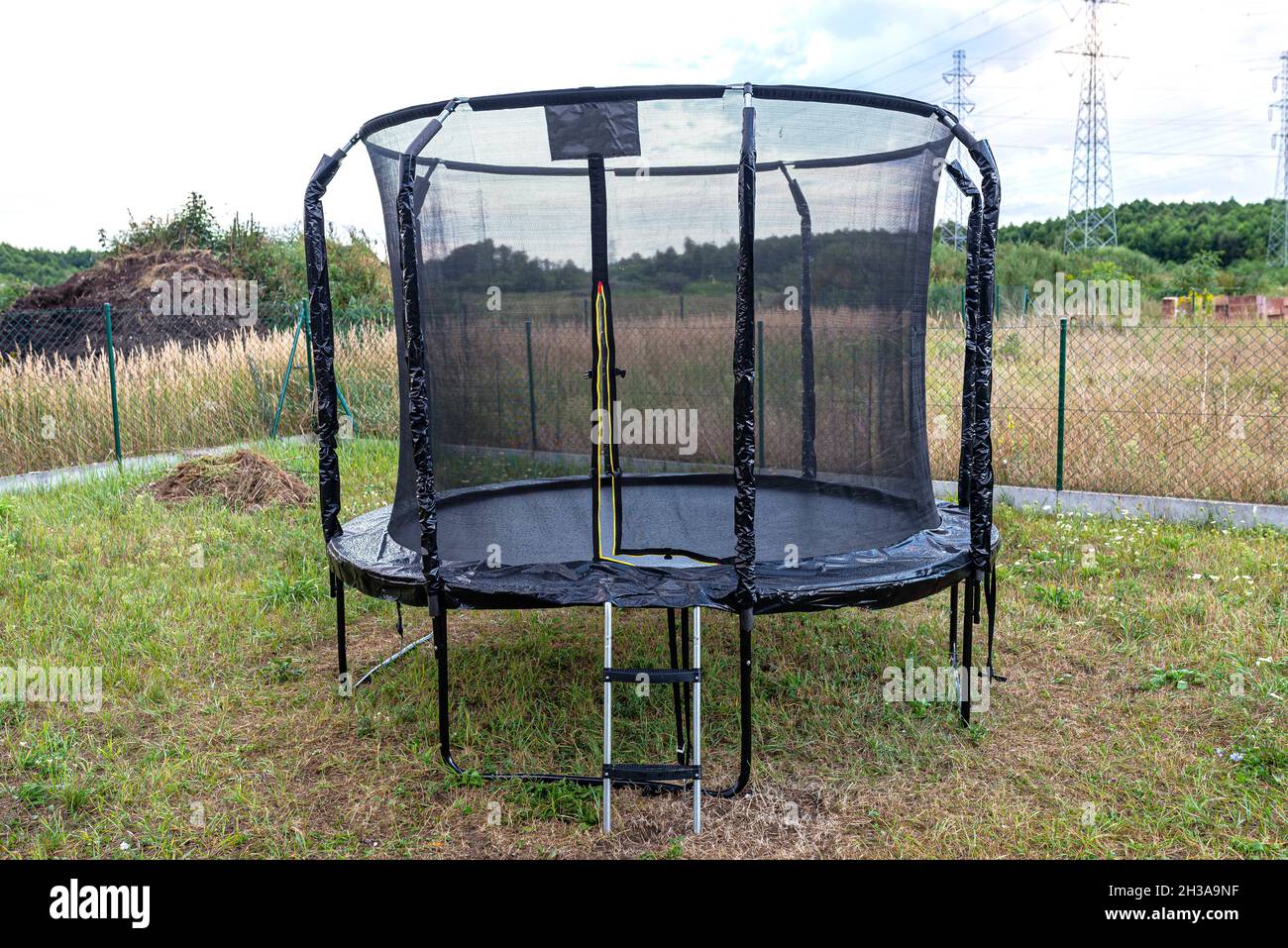 Großes Kinderspringtrampolin mit Schutznetz und offenem Reißverschluss, im Garten stehend. Stockfoto