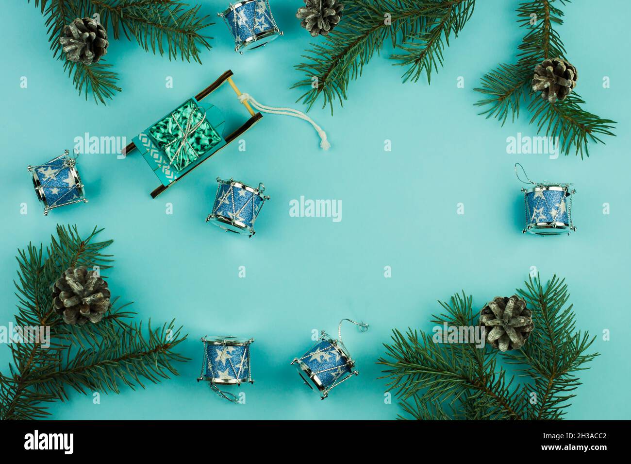 Blauer weihnachtlicher Hintergrund mit Fichtenzweigen und Zapfen, Weihnachtsspielzeug zur Dekoration, Schlitten mit Geschenk, traditionelle Weihnachtstrommeln. Draufsicht Stockfoto