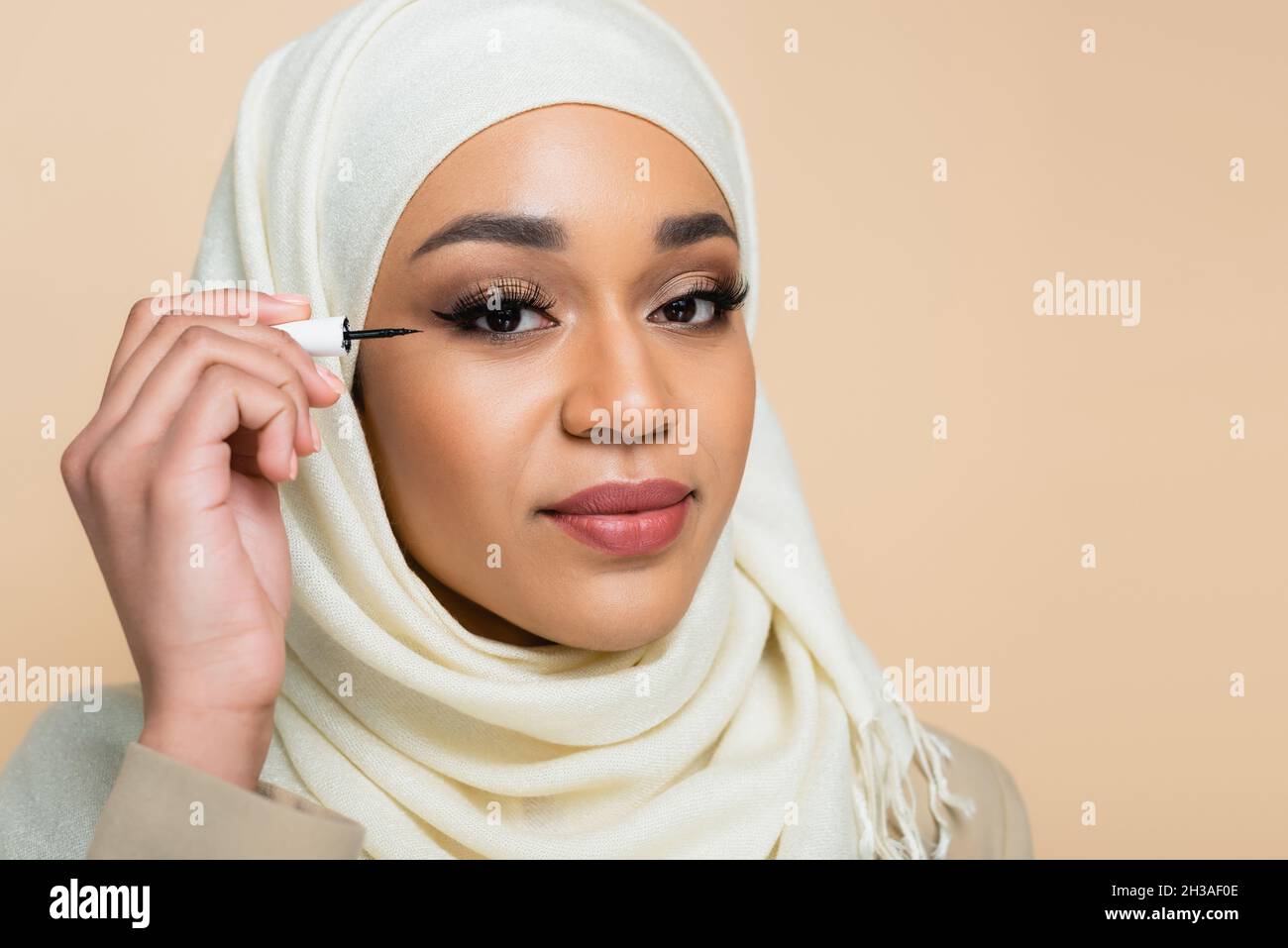 Junge muslimische Frau im Hijab, die schwarze Augenlinse auf Beige auftragen Stockfoto