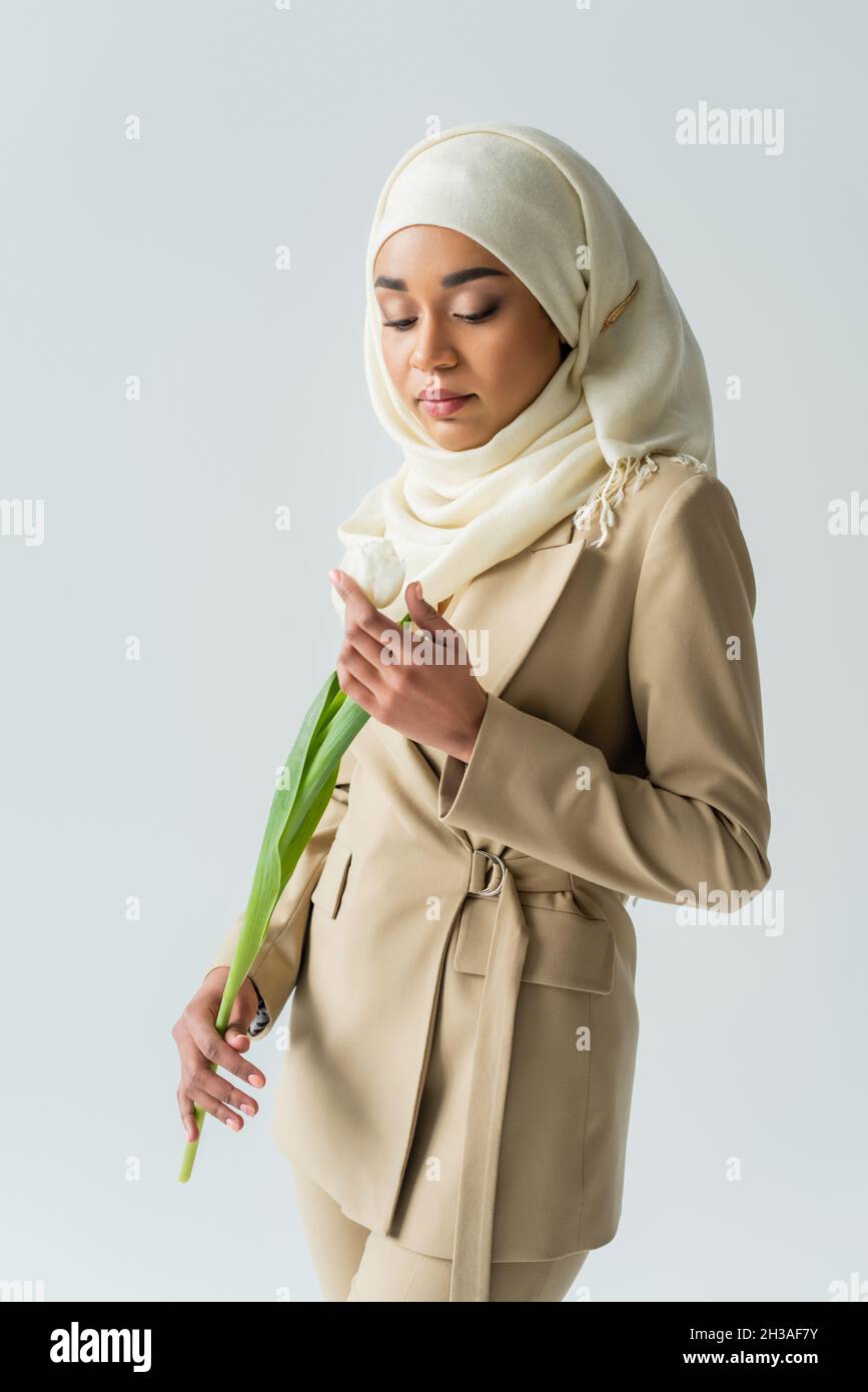 muslimische junge Frau in Hijab, die Tulpe isoliert auf Grau betrachtet Stockfoto