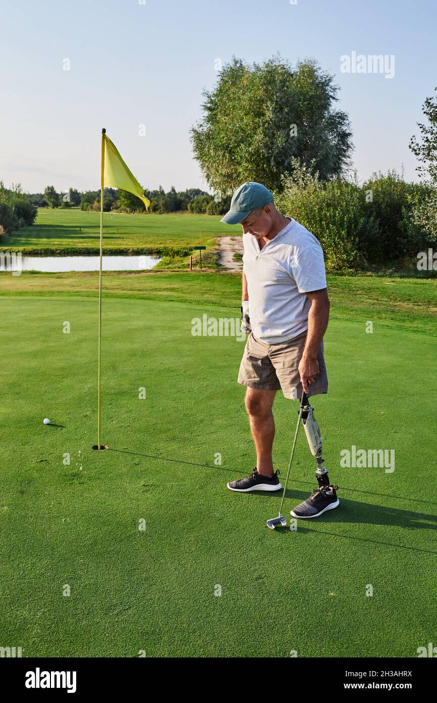 Erwachsene Mann mit einem künstlichen Bein Golf im Freien auf dem grünen Golfplatz spielen und lebt ein volles Leben. Golf für Menschen mit Behinderungen Stockfoto