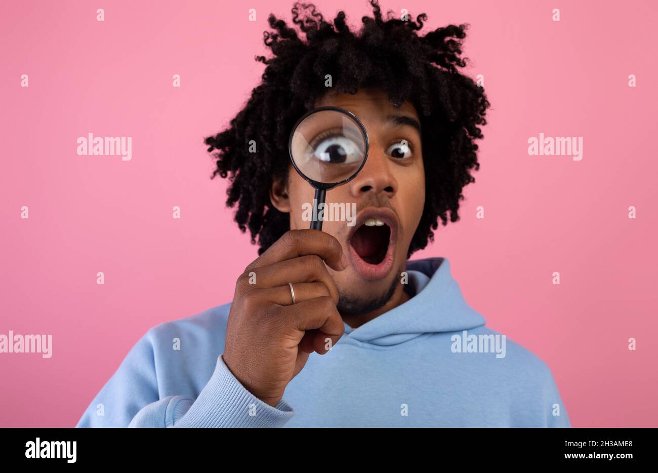 Schockiert schwarz teen Kerl suchen durch Lupe auf rosa Studio Hintergrund. Geheimnis, Zweifel Konzept Stockfoto