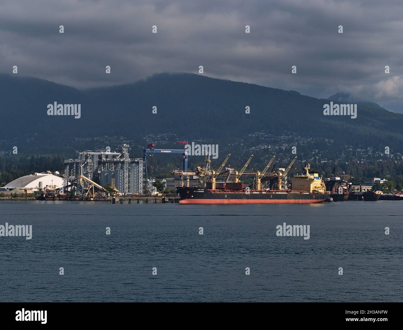 Bulk Carrier DL Lavender Liegeplatz im Hafen in Vancouver Nord für die Verladung vor dem Industriegebiet mit Tanks und Kran und Berge im Hintergrund. Stockfoto