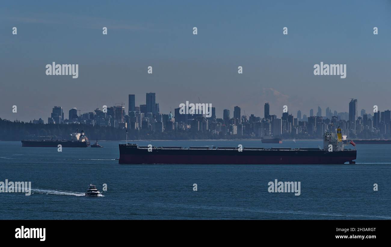 Frachtschiffe passieren die Innenstadt von Vancouver am Burrard Inlet, vom Lighthouse Park aus gesehen, mit Skycreapes und Mount Rainier im Hintergrund. Stockfoto