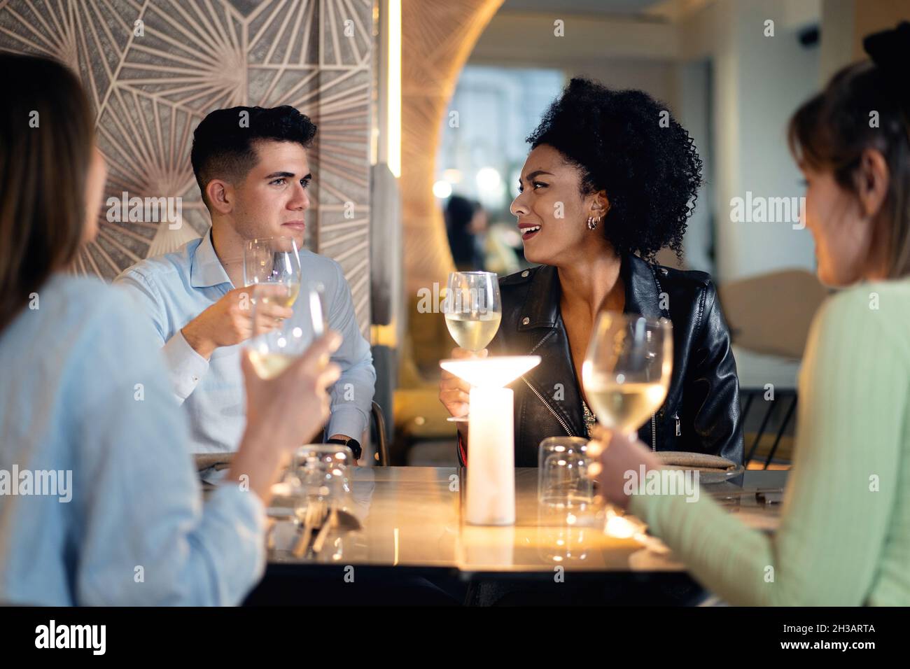 Vielfältige Gruppe von Freunden, die sich unterhalten und Weißwein trinken. Schöne junge Leute haben Spaß in der stilvollen Bar/Restaurant. Stockfoto