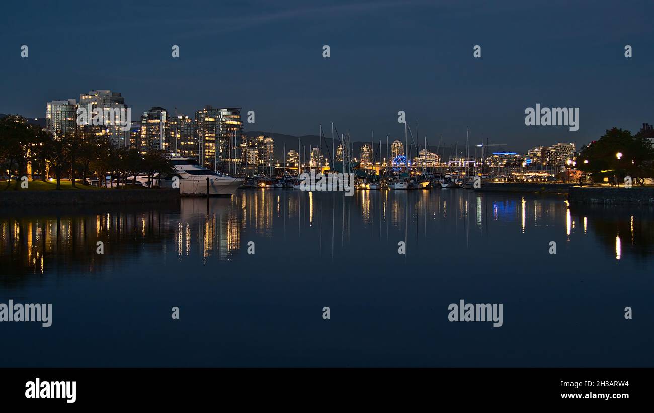 Atemberaubende Aussicht auf die Bucht von False Creek bei Nacht mit der beleuchteten Skyline von Vancouver Downtown, die sich im ruhigen Wasser mit dem Yachthafen und den Jachtbooten widerspiegelt. Stockfoto