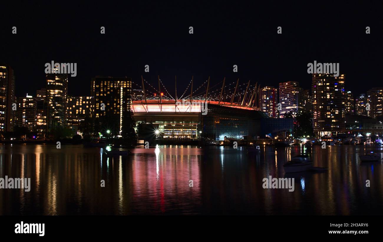 Wunderschöner Blick auf die False Creek Bay, Vancouver Downtown mit rotem Schimmer des beleuchteten BC Place Stadions, der sich im glatten Wasser und den Gebäuden widerspiegelt. Stockfoto