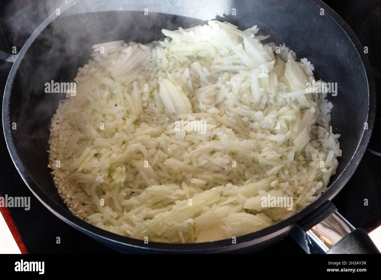 Fein gehackte Zwiebeln, die in einer tiefen Bratpfanne in der heimischen Küche anbraten Stockfoto