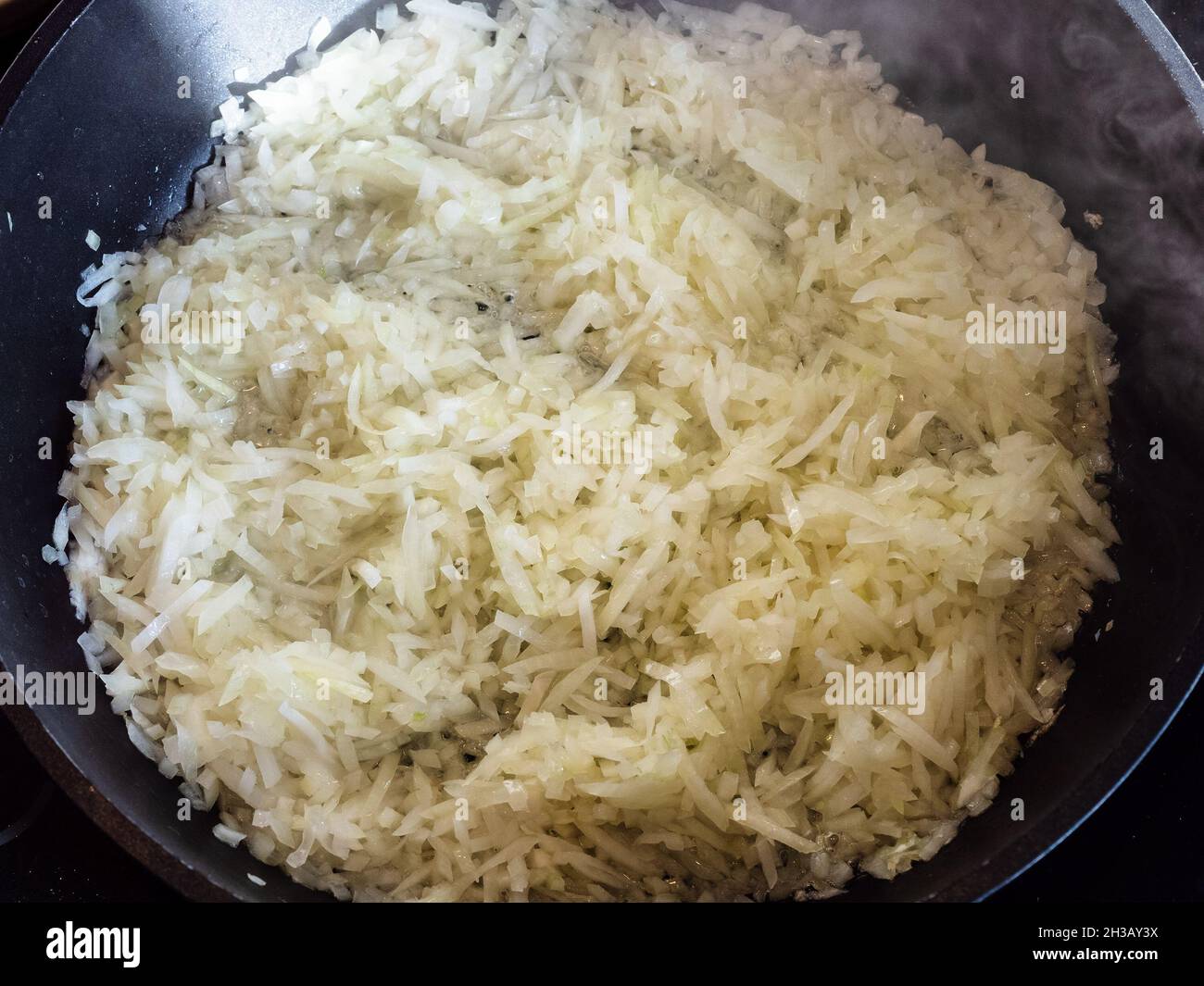 Draufsicht auf fein gehackte Zwiebeln Braten in der Frittierpfanne in der heimischen Küche Stockfoto