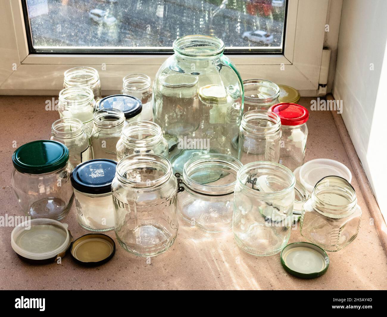 Verschiedene leere Gläser aus reinem Glas, die für die Konservierung auf der Fensterbank der städtischen Wohnküche vorbereitet wurden, die am sonnigen Herbstabend von der Sonne beleuchtet wird Stockfotografie