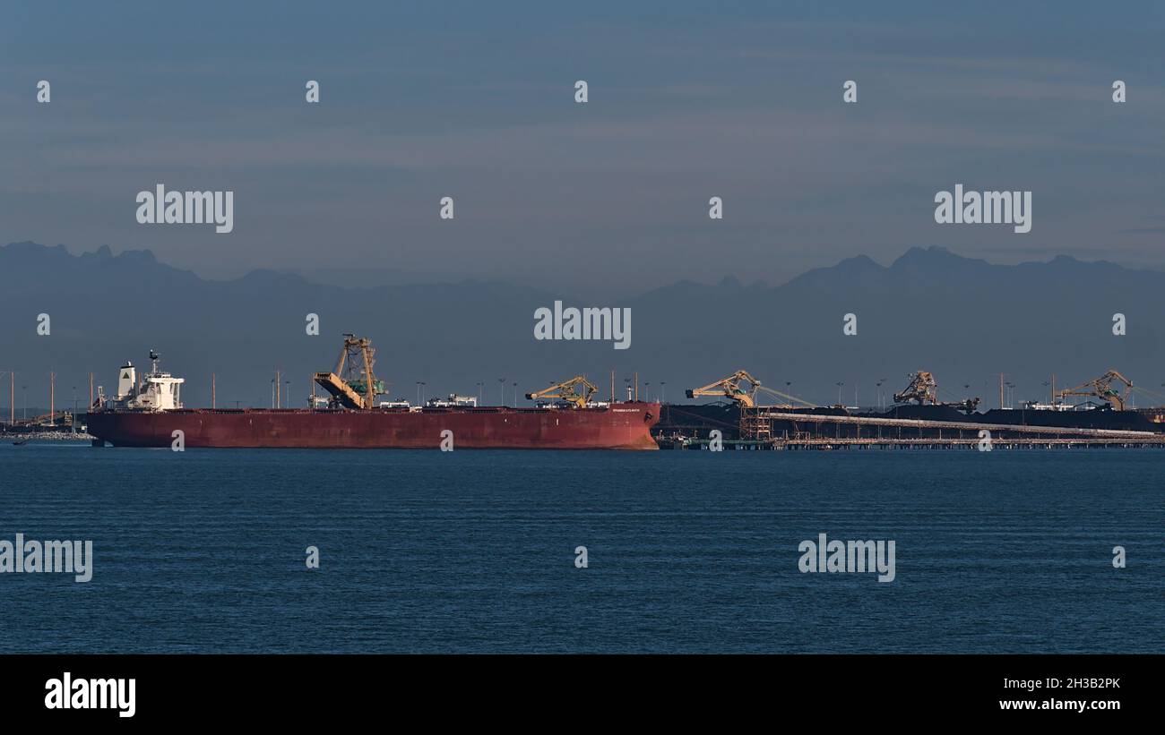 Bulk Carrier Hyundai Atlantic lädt Kohle bei Roberts Bank Superport, Teil von Vancouver Harbour, mit den Silhouetten der Berge im Hintergrund. Stockfoto