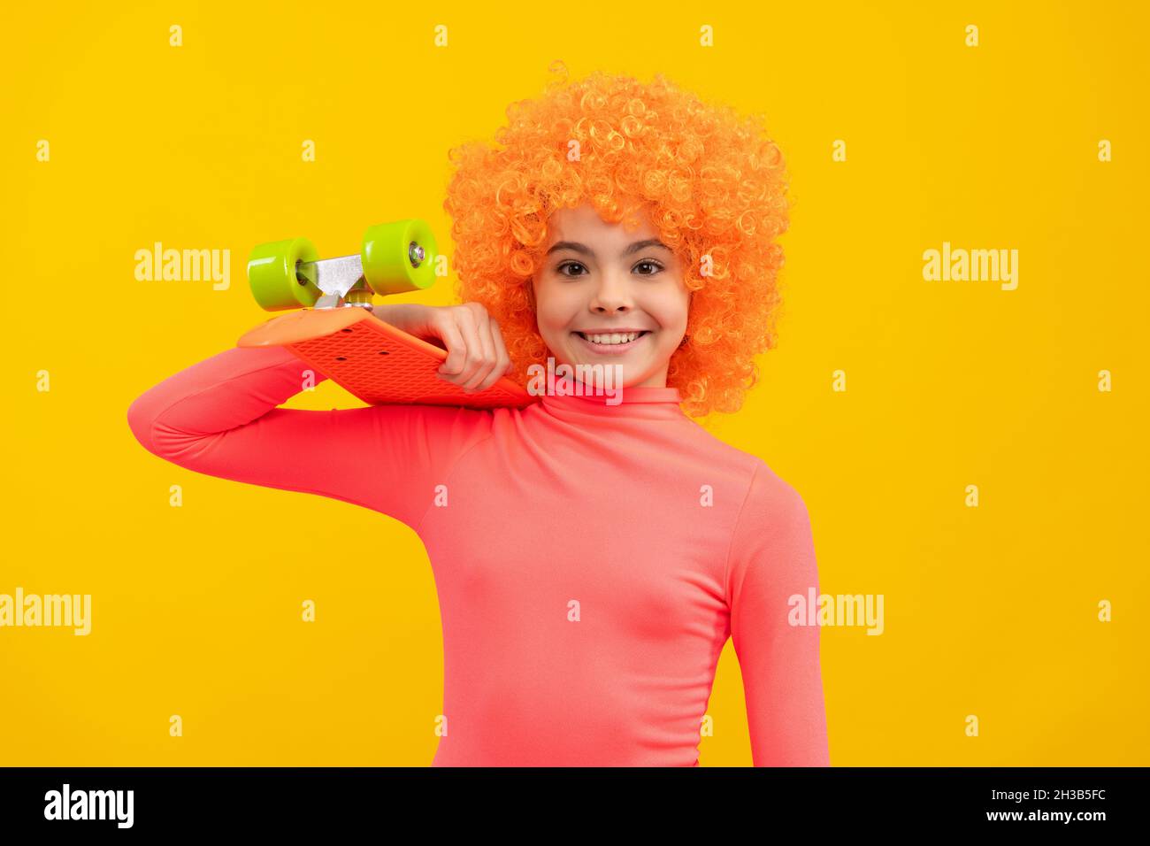 Glückliches Mädchen Kind mit orangefarbenen Haaren in rosa Poloneck Lächeln hält Pennyboard, Pennyboard Stockfoto