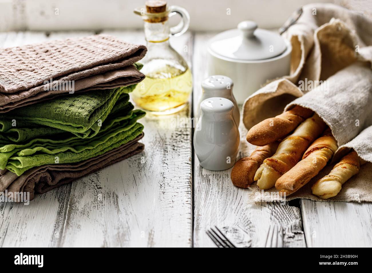 Bunte Baumwollservietten, Besteck und Grissini italienische Brotstangen auf weißem, rustikalem Hintergrund. Speicherplatz kopieren. Stillleben Stockfoto