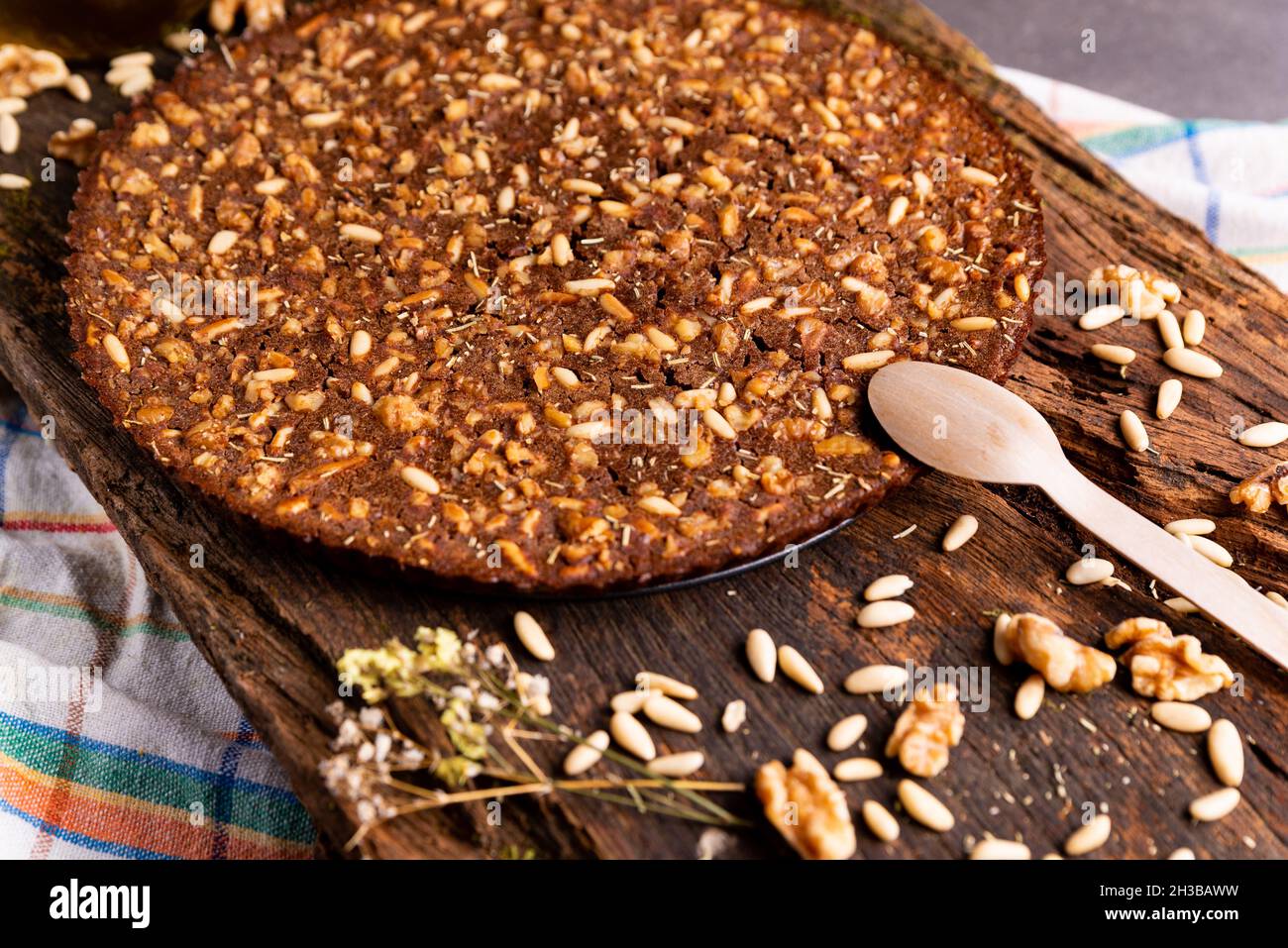 Nahaufnahme des traditionellen Castagnaccio-Kuchens, einer klassischen italienischen glutenfreien Herbstkuchen auf einem Holztisch aus Kastanienmehl, Pinienkernen, Rosmarin und Stockfoto
