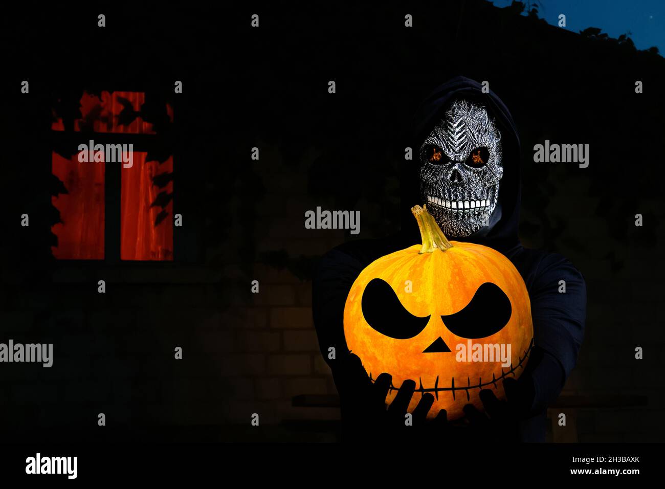 Nahaufnahme des grimmigen Reaper. Mann in Totenmaske mit Feuerflamme in den Augen auf dunklem nächtlichen Hintergrund. Faschingskostüm, gruselige Zähne. Halloween-Holida Stockfoto