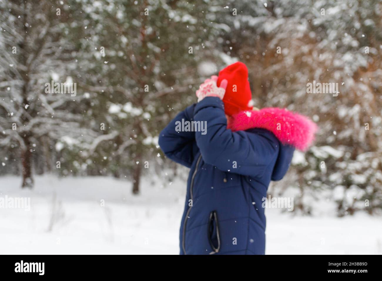 Defocus Porträt von präteen glücklich Mädchen außerhalb setzen roten warmen Hut auf Natur Winter verschneiten Wald Hintergrund. Hübsches Kind im Freien, kaltes Wetter. Cauc Stockfoto
