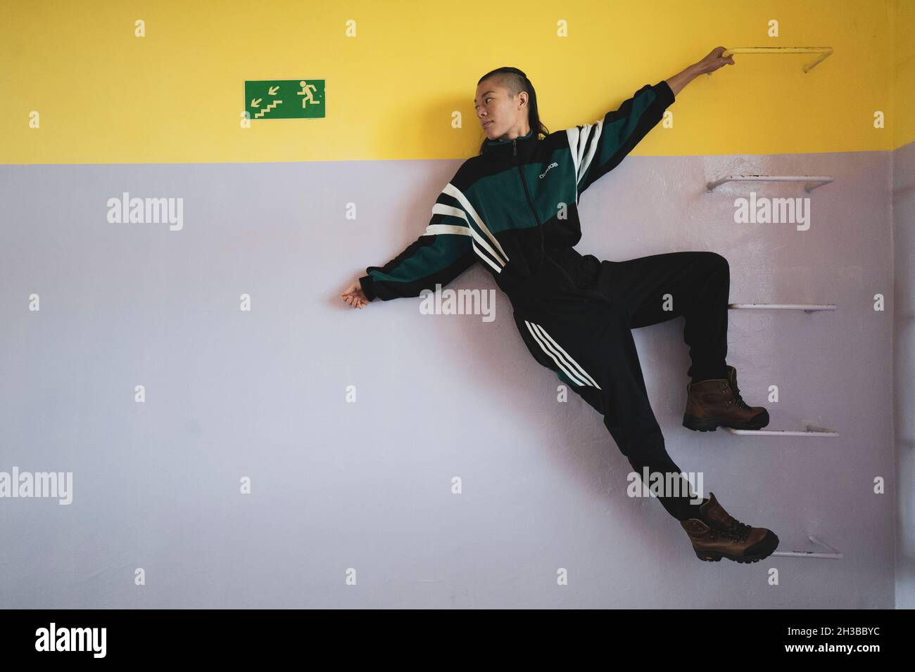 In der Pastellschule hängt eine athletische androgyne starke Frau an den Gittern Stockfoto