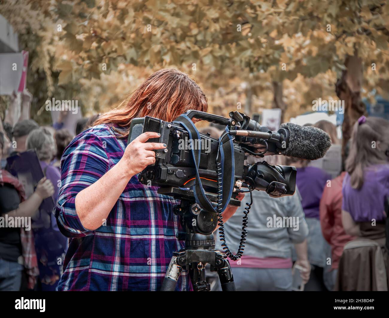 Weibliche Fernsehvideografin mit professioneller Kamera, die am Herbsttag bei überfüllten Protesten filmte - Nahaufnahme Stockfoto