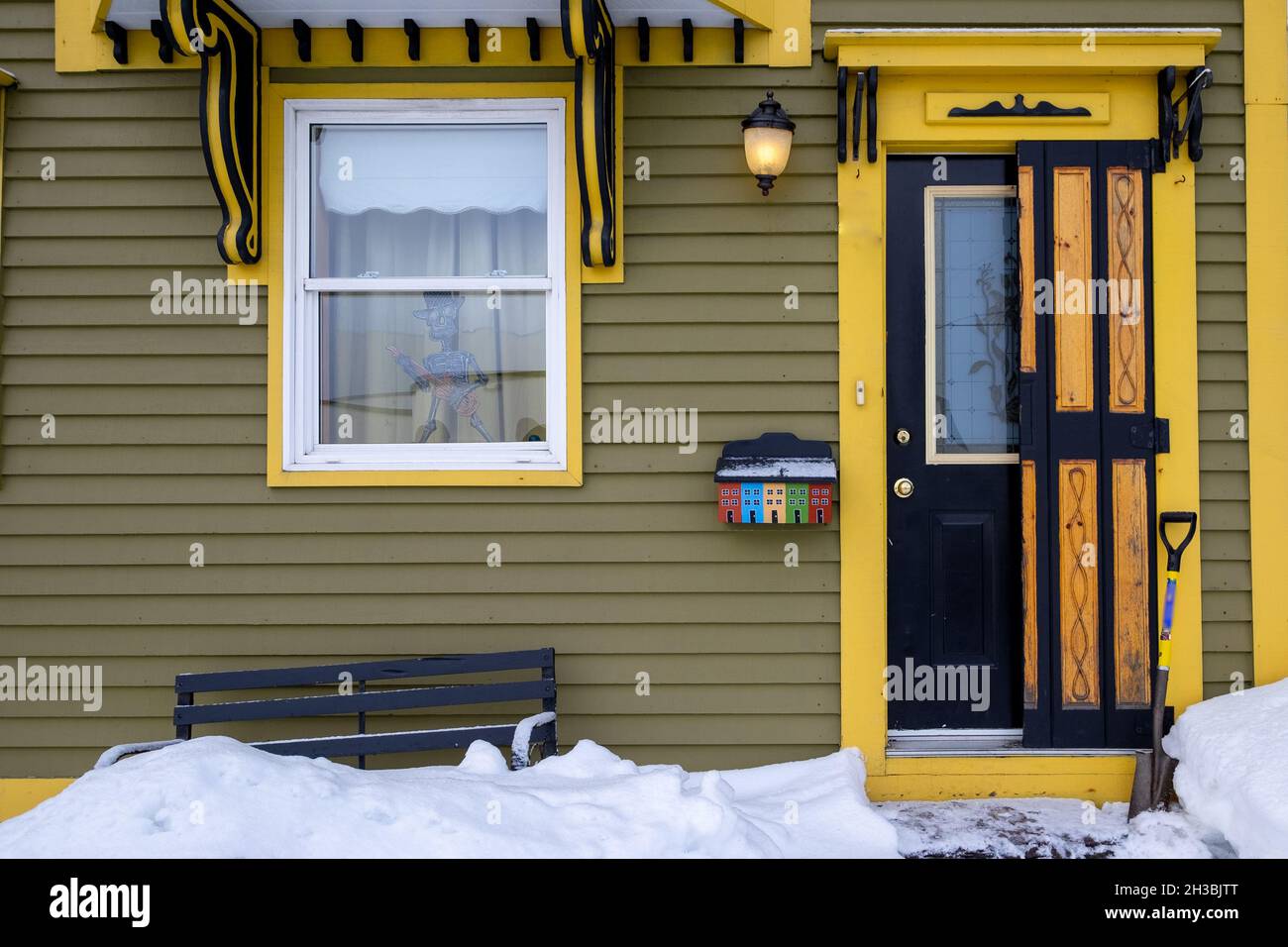 Eine schwarze Vintage-Tür mit gelber Zierleiste auf einem grünen Holzhaus. Die Tür hat ein Glasfenster mit Holzfenster. Über der Tür befinden sich dekorative Abziehbilder. Stockfoto