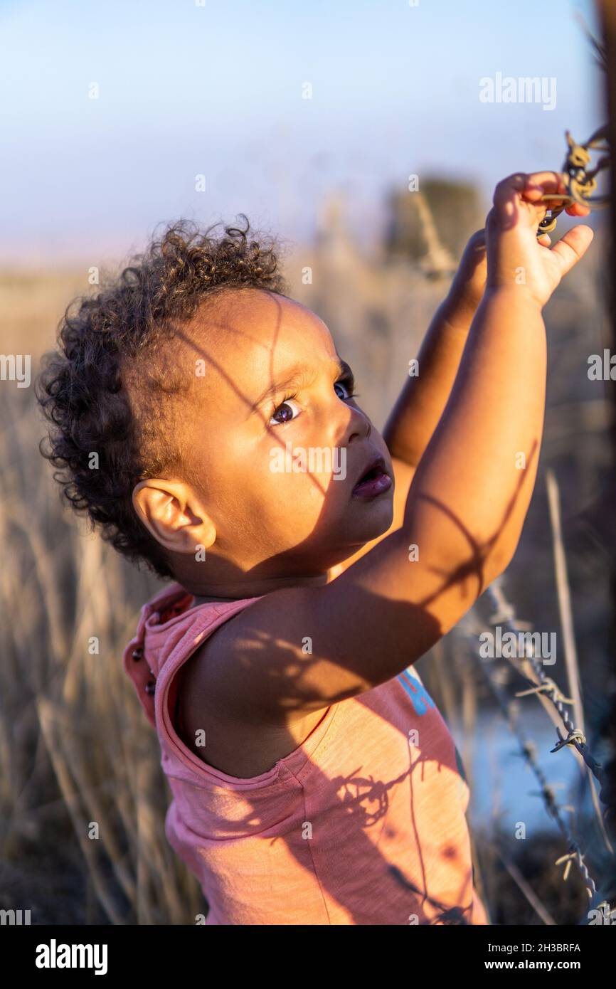 Ein Porträt eines äthiopischen gemischtkindlichen, interracial kindlichen Kleinkindes mit gemischtem Etnismus, das einen Stacheldrahtzaun hält und besorgt und traurig aussieht. Stockfoto