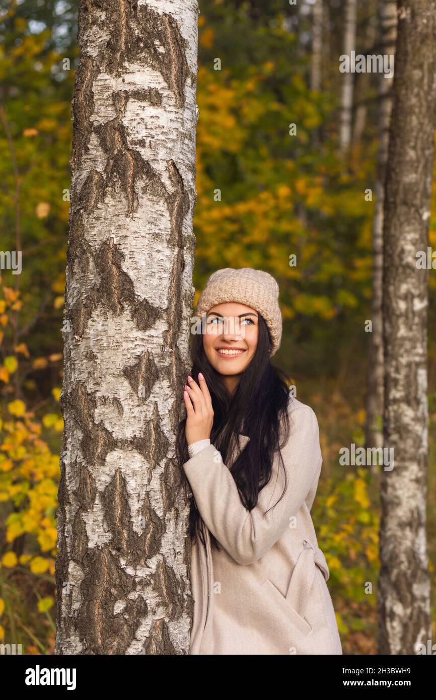 Porträt einer fröhlichen jungen Frau, die im Herbstpark genießt. Schöne Brünette Mädchen im Herbst grauen Mantel und gestrickten Hut. Entspannen Sie sich in der Natur. Stockfoto