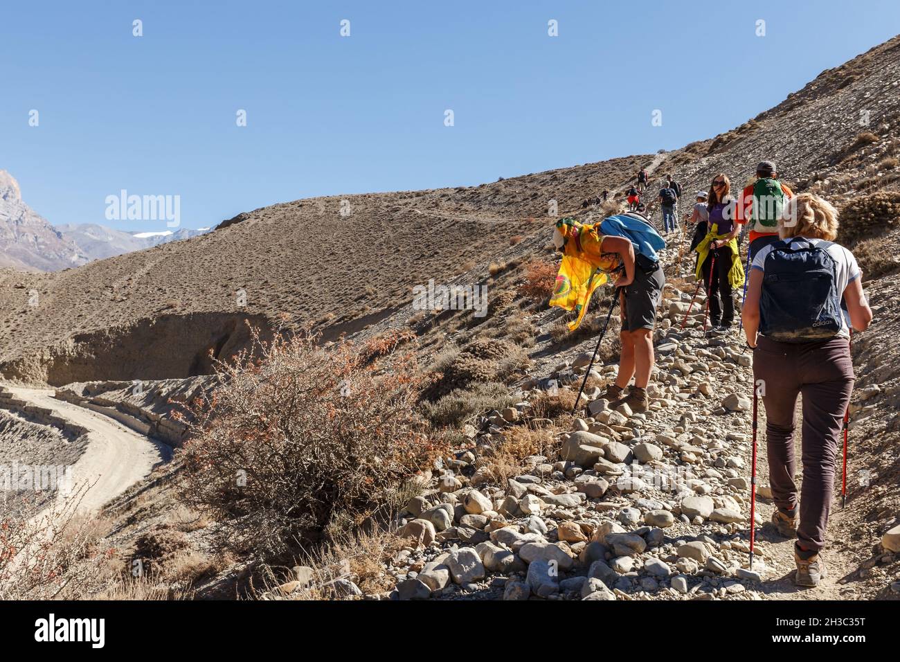Kagbeni, Mustang District, Nepal - 19. November 2016: Eine Gruppe von Touristen läuft auf einem schmalen Bergweg. Eine Frau wurde krank und ruht sich aus. Stockfoto