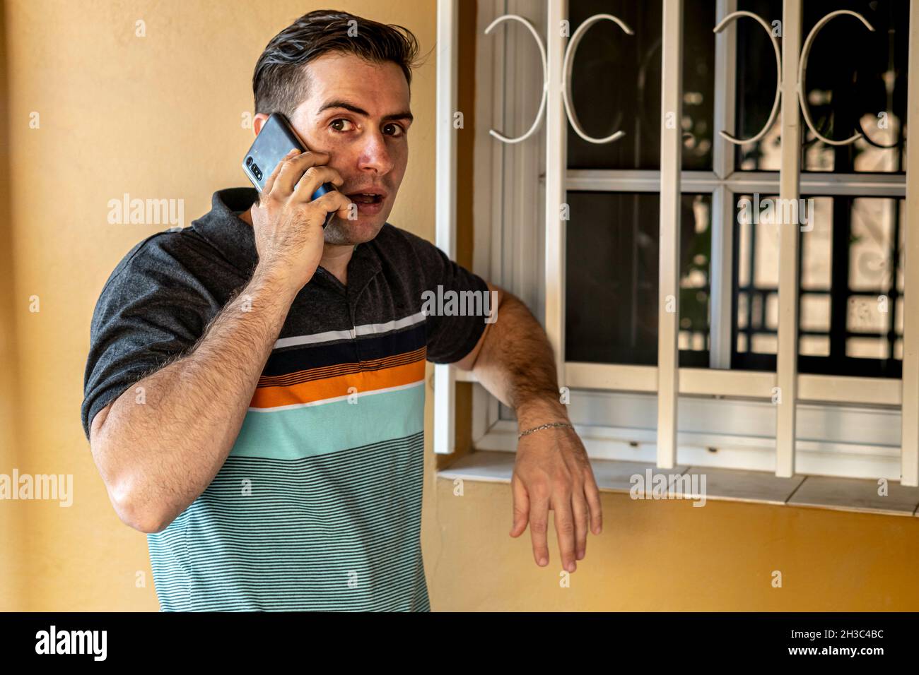 Seriöse junge hispanische Kerl reden auf seinem Telefon lehnt sich an ein Fenster von draußen Stockfoto