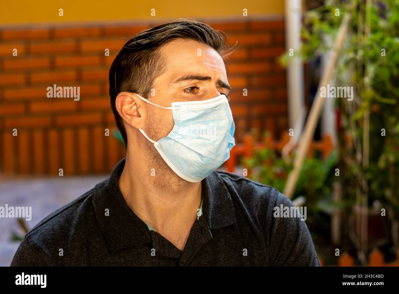 Junger hispanischer Kerl, der eine Damenmaske im Freien trägt und wegschaut Stockfoto