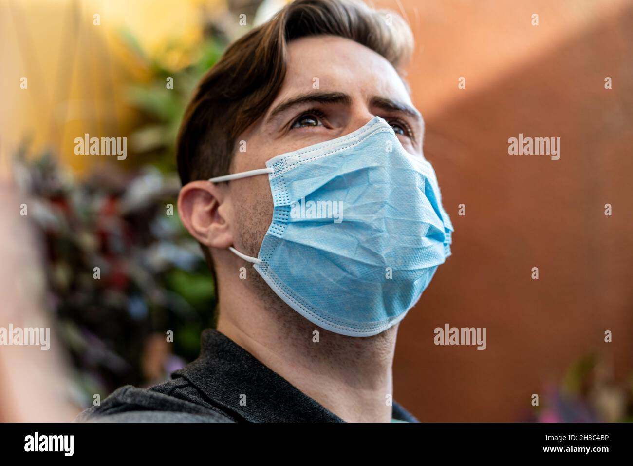 Junger hispanischer Kerl, der eine Damenmaske im Freien trägt und wegschaut Stockfoto