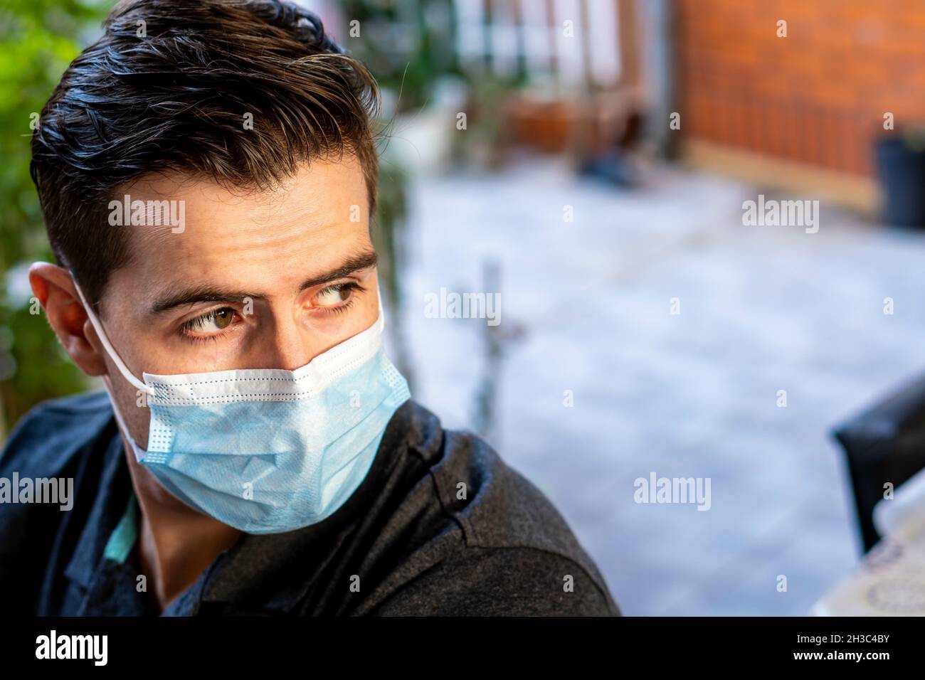 Junger hispanischer Kerl, der eine Damenmaske im Freien trägt und wegschaut Stockfoto