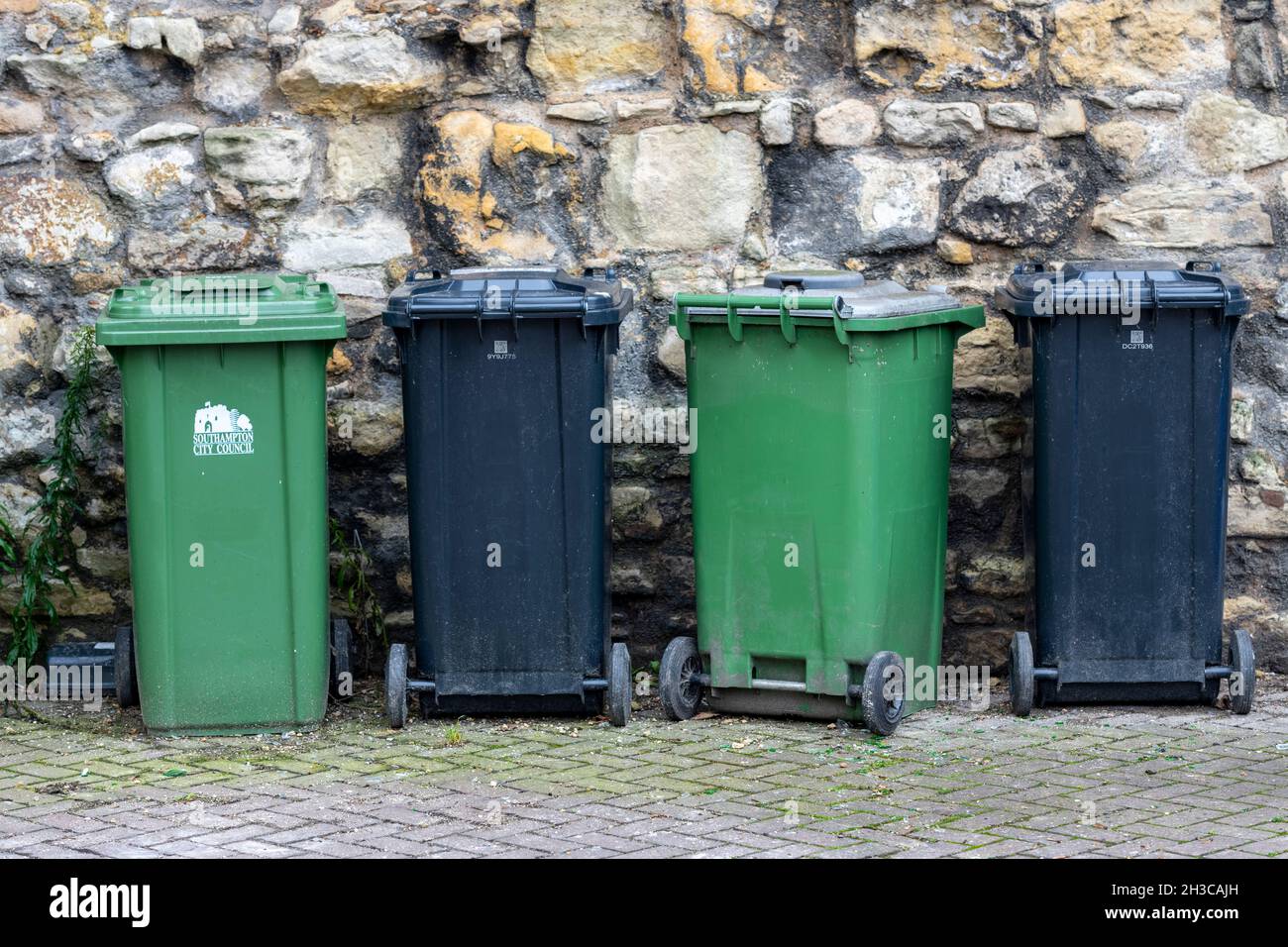 Mülltonnen in einer Reihe, Reihe von Mülltonnen, Mülltonnen, Abfallrecycling-Behälter, Mülltonnen bereit zur Sammlung. Schwarze und grüne Kunststoffabfallbehälter Stockfoto