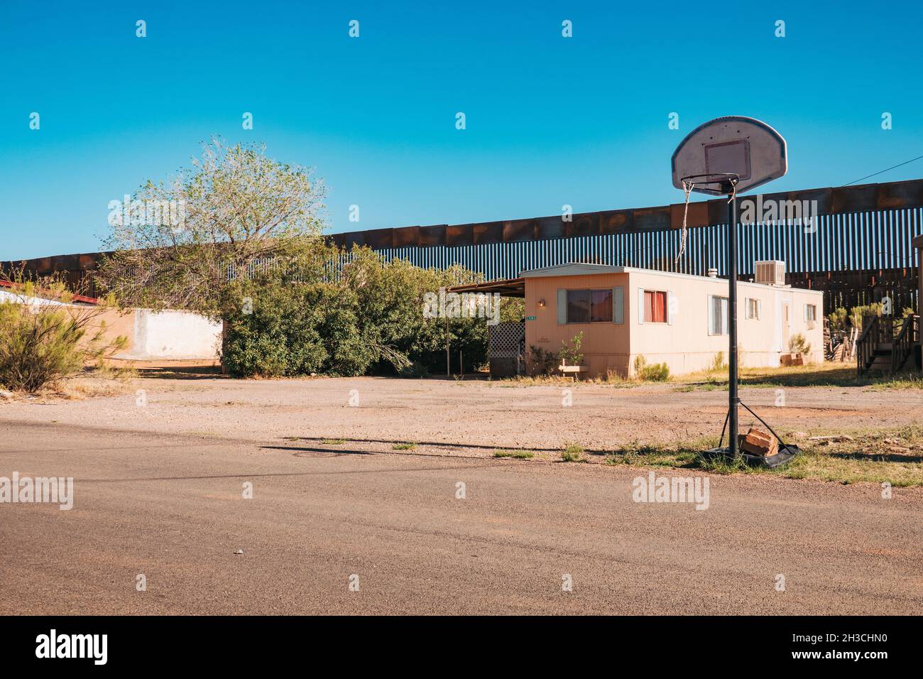 Ein Basketballkorb auf der Straße in der US-Grenzstadt Naco, Arizona. Dahinter ragt die hohe, verrostete Stahlgrenzmauer zwischen den USA und Mexiko Stockfoto