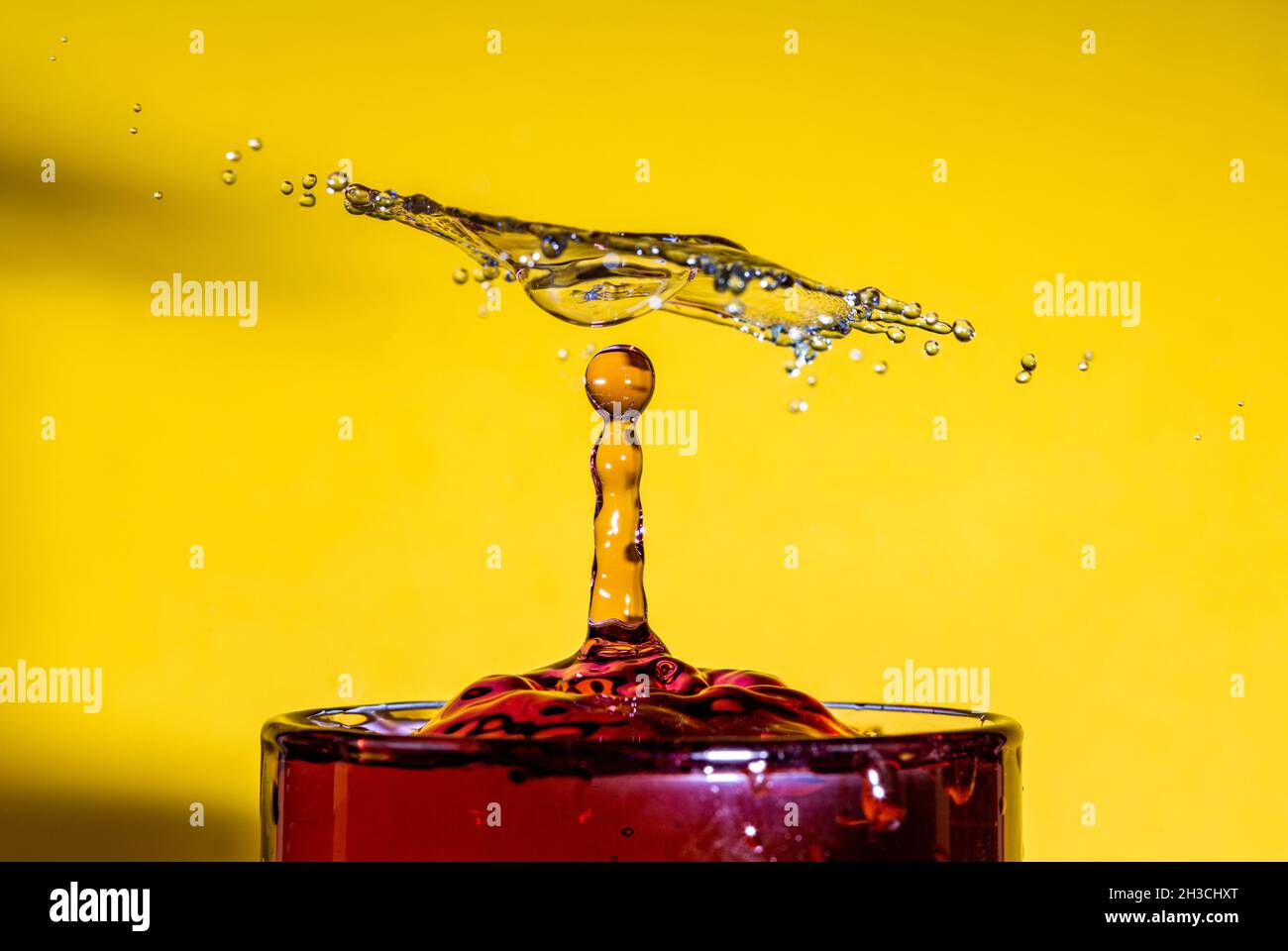 Abstrakte Ansicht eines Wassertropfens, der auf ein Glas roten Wassers fällt. Stockfoto