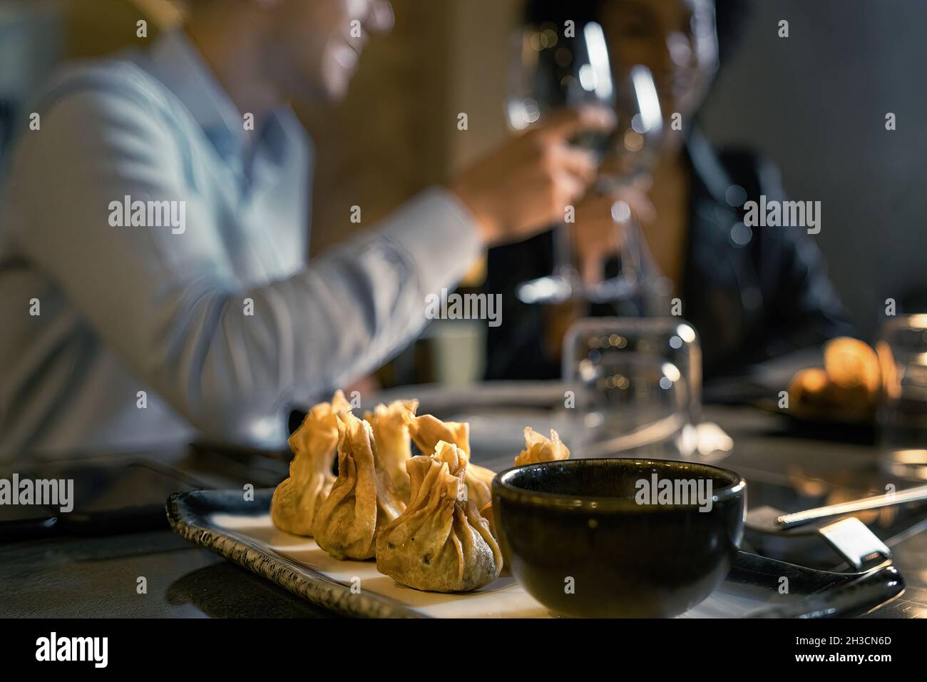 Restauranttisch mit Dim Sum, traditionelle chinesische Knödel, im Vordergrund. Im Hintergrund entkokkt ein paar junge Leute trinken Whi Stockfoto