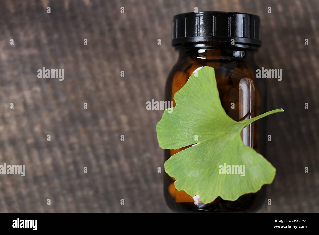 Ginkgo biloba Pillen.Braunes Glas mit homöopathischen Pillen mit Ginkgo-Extrakt und Ginkgo-Blätter auf hölzernen Hintergrund. Alternative Medizin und Stockfoto