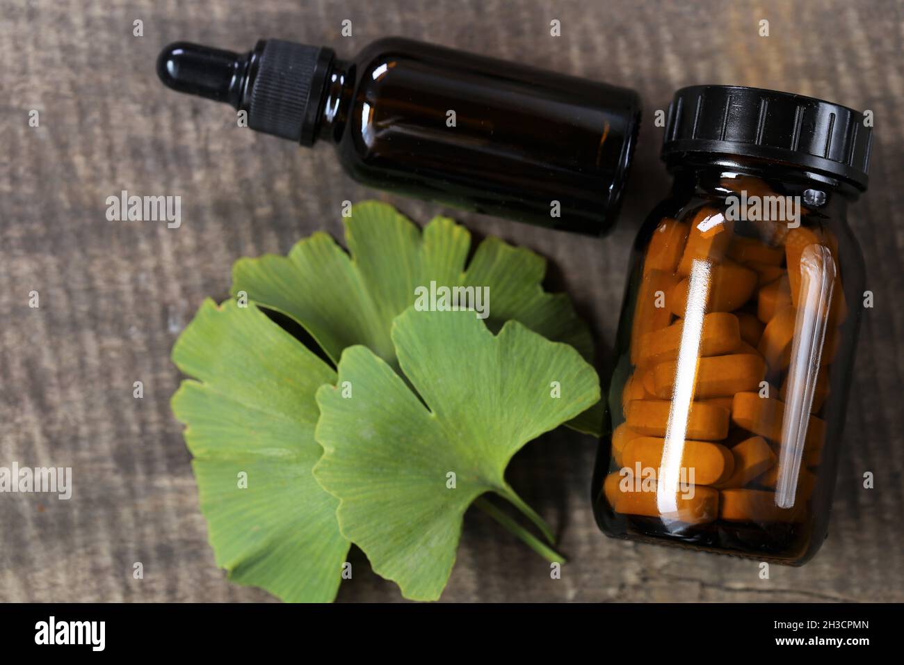 Ginkgo biloba .Braunes Glas mit homöopathischen Pillen mit Ginkgo-Extrakt und Ginkgo-Blätter auf hölzernen Hintergrund. Alternative Medizin und Homöopathie Stockfoto
